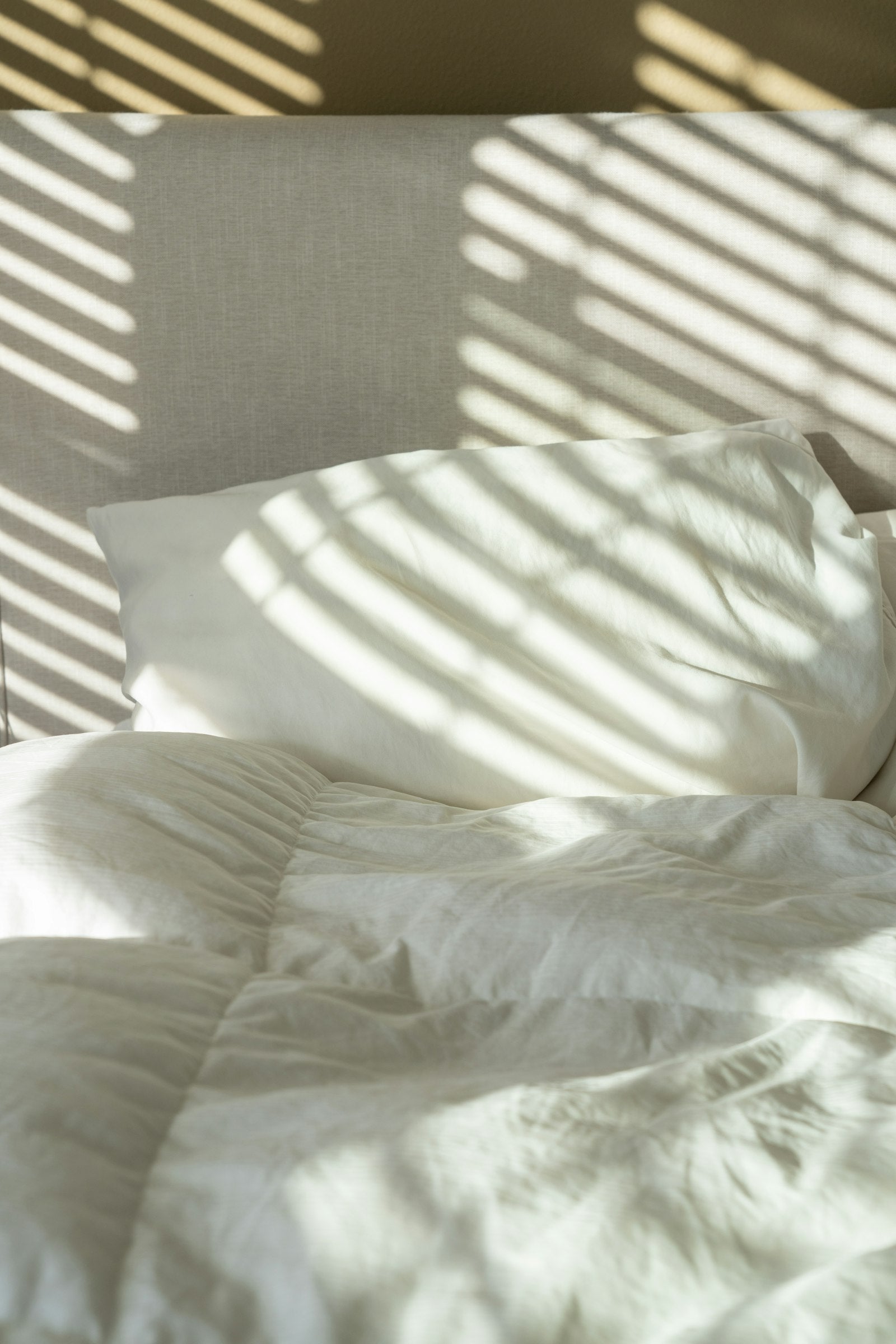 Opgemaakt bed met zacht crèmekleurig dekbed in warm ochtendlicht — welk dekbed kiezen